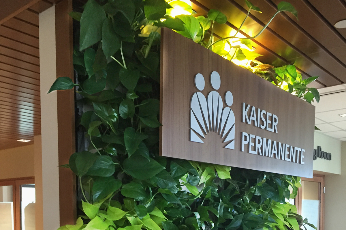 Green tropicals in a living wall serve as a backdrop to a Kaiser Permanente health care sign.
