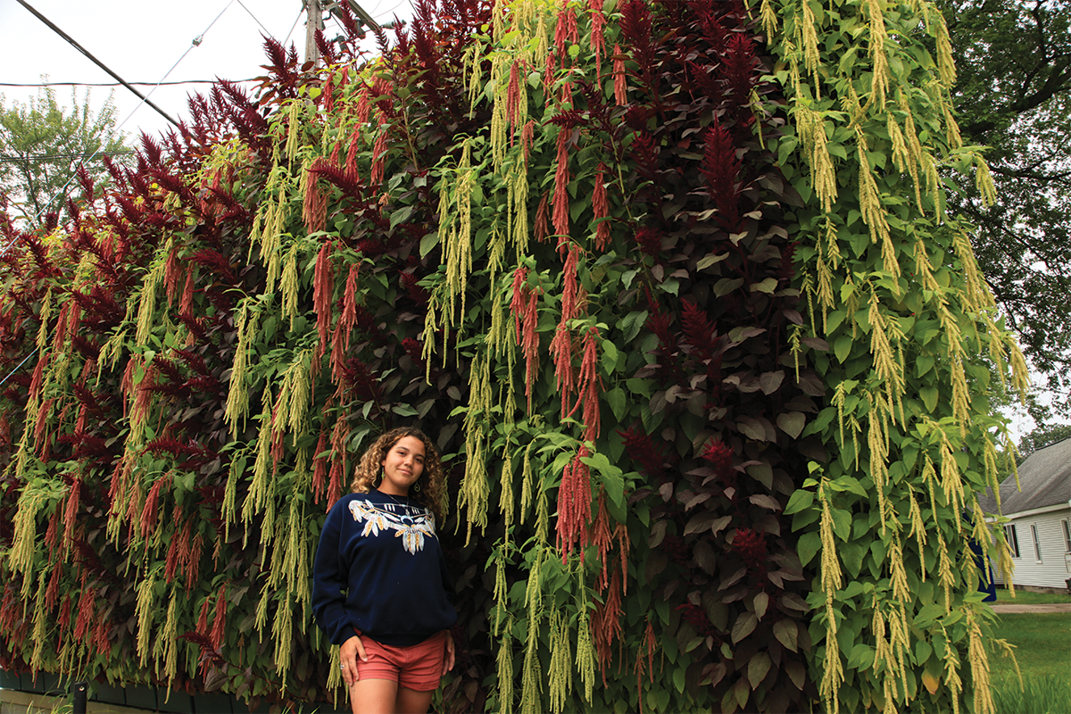 Woman standing next to a tall living wall with dangling amaranthus