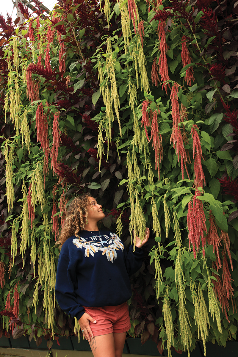 Woman standing next to and fondling a living wall with red amaranthus