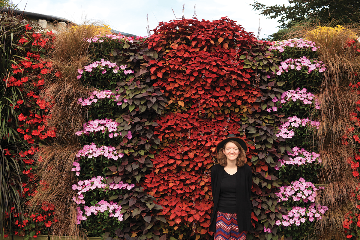 Woman in a stylish hat standing in front of a vibrant, red, pink, and violet living wall